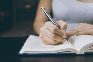 a person writing on a book with a pen.