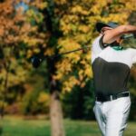 Golfer finishing a full swing on a green fairway in fall colors, a visual example of golfing with sciatica.
