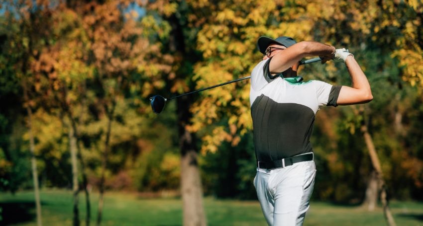 Golfer finishing a full swing on a green fairway in fall colors, a visual example of golfing with sciatica.