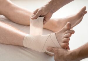 Clinician wraps an elastic bandage around a patient’s ankle and foot for support during peroneal tendonitis recovery time and return to activity.