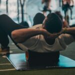 Spinal decompression workout in a gym, showing a person lying on a mat with a foam roller under the upper back, hands behind the head, using gentle pressure to relieve back tightness.