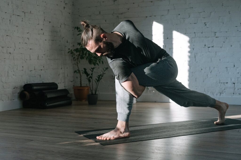 Stretching exercises for the spine as a man performs a deep lunge and twist on a yoga mat in a sunlit studio.