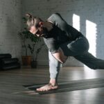 Stretching exercises for the spine as a man performs a deep lunge and twist on a yoga mat in a sunlit studio.