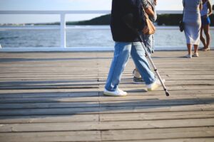 Feeling off balance while walking, person using a cane on a wooden boardwalk near the water