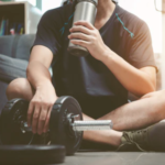 How much protein for post workout as a man drinks a protein shake while resting after lifting dumbbells