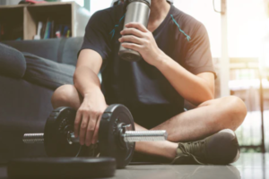 How much protein for post workout as a man drinks a protein shake while resting after lifting dumbbells