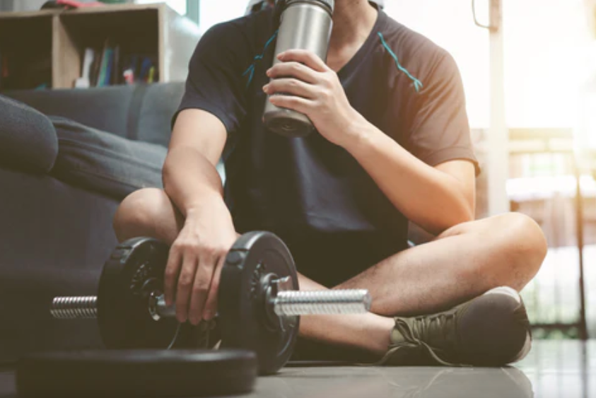 How much protein for post workout as a man drinks a protein shake while resting after lifting dumbbells
