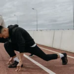 Stretching exercises for runners on a track, runner holding a deep lunge warm-up stretch while a training partner stands nearby