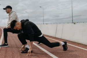 Stretching exercises for runners on a track, runner holding a deep lunge warm-up stretch while a training partner stands nearby