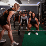 Coach cues athletes during a workout routine for athletes as they set up barbell deadlifts in a training gym.