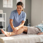A physical therapist in a modern clinic is gently supporting and mobilizing a patient's injured ankle while the patient lies on a treatment table, focusing on restoring range of motion and reducing pain from the sprained ankle. The therapist's careful approach aims to prevent further injury and aid in the rehabilitation process for the patient's ankle function.