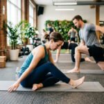Man and woman doing hip mobility exercises together on gym mats