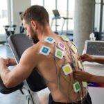 Physical therapist performing neuromuscular electrical stimulation (NMES) with multiple electrode pads on a patient's back